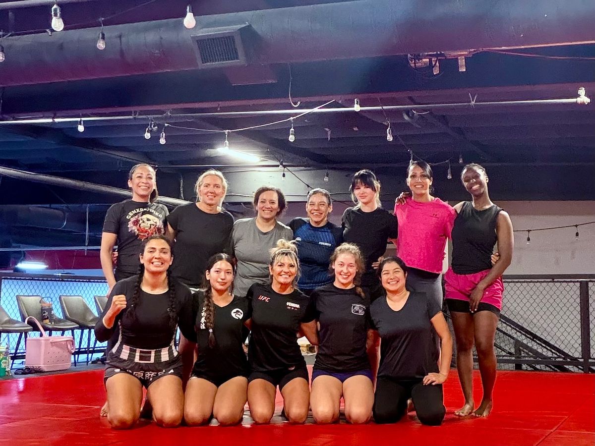 A group of women smiling together on the mats after class