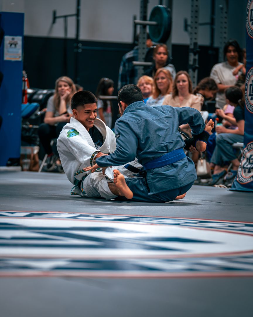 Two jiu-jitsu players in gis grappling while members watch